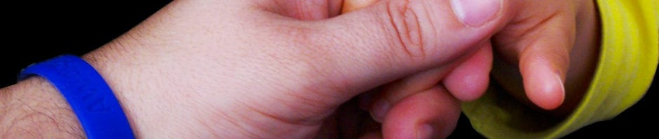 adult hand with an autism awareness wrist band holding an autistic baby hand