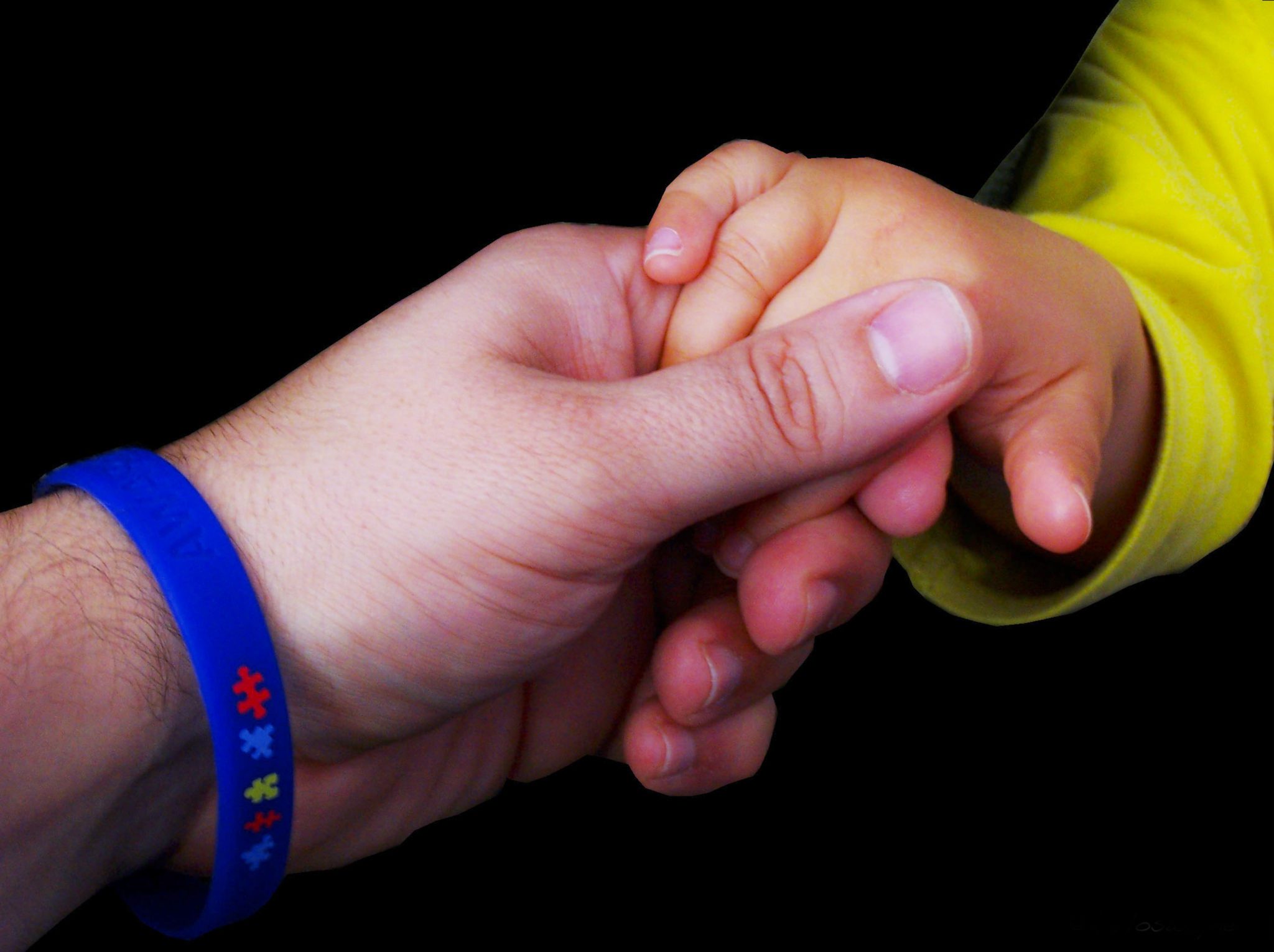 adult hand with an autism awareness wrist band holding an autistic baby hand