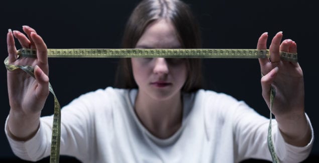 Teen girl in shadows stretching out tape measure in front of her face