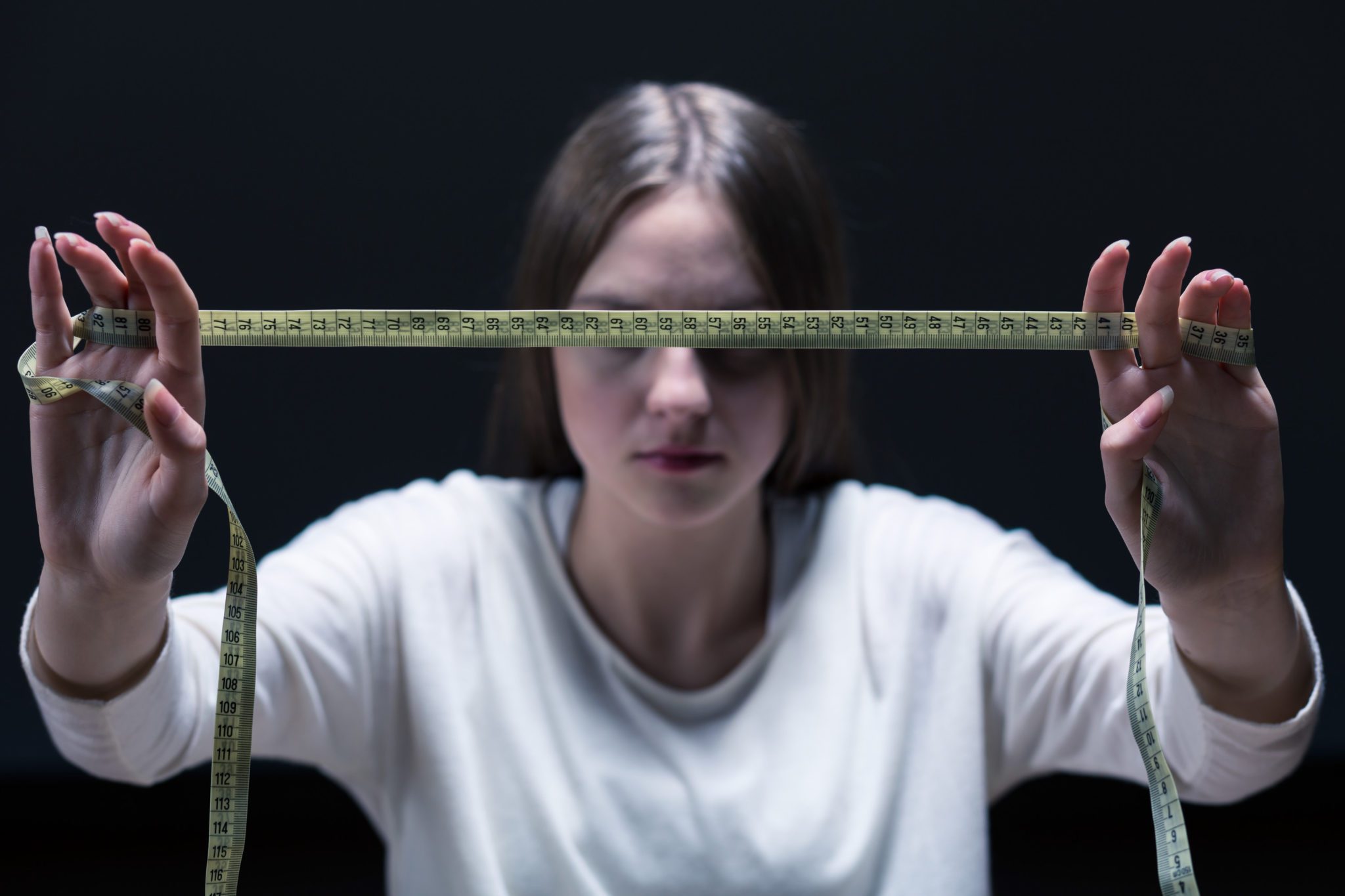 Teen girl in shadows stretching out tape measure in front of her face