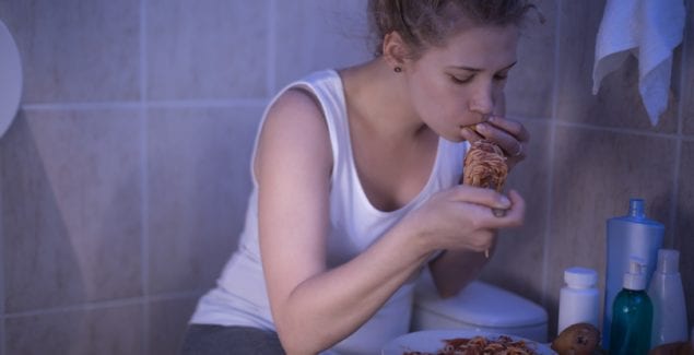 Teen girl hiding and sitting in a dark bathroom while bingeing on spaghetti