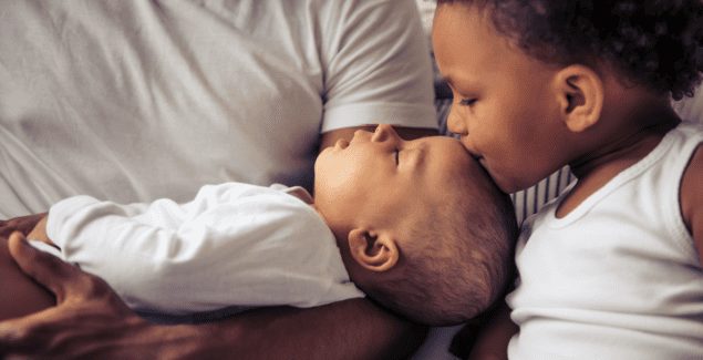 Beautiful young afro american family spending time together. little baby is sleeping in dad's arms while her sister is kissing her