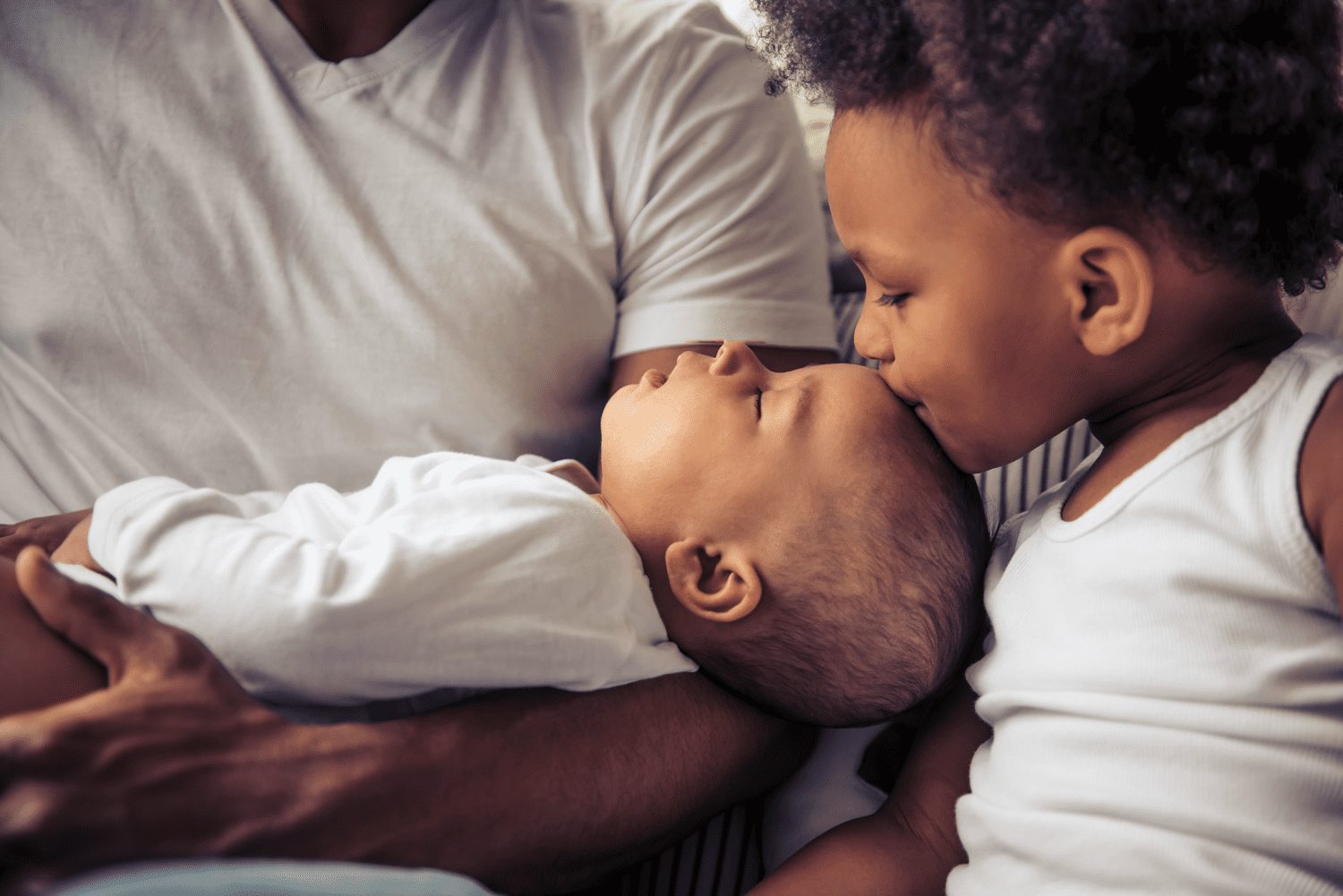 Beautiful young afro american family spending time together. little baby is sleeping in dad's arms while her sister is kissing her