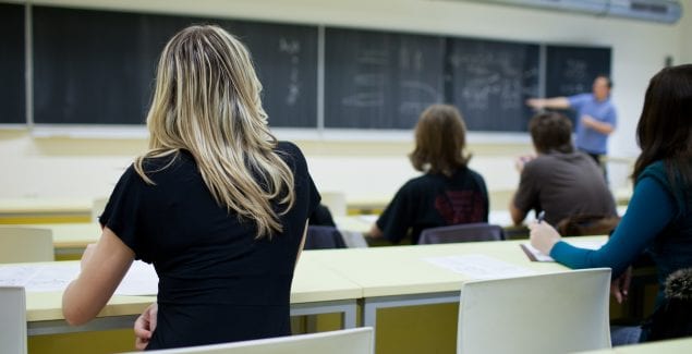 behind shot of female college student sitting in a classroom full of students during class