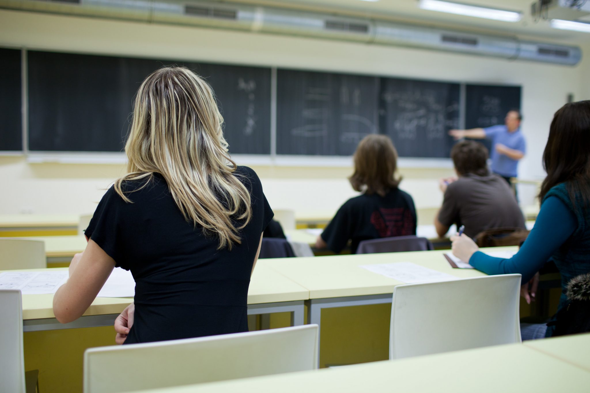 behind shot of female college student sitting in a classroom full of students during class