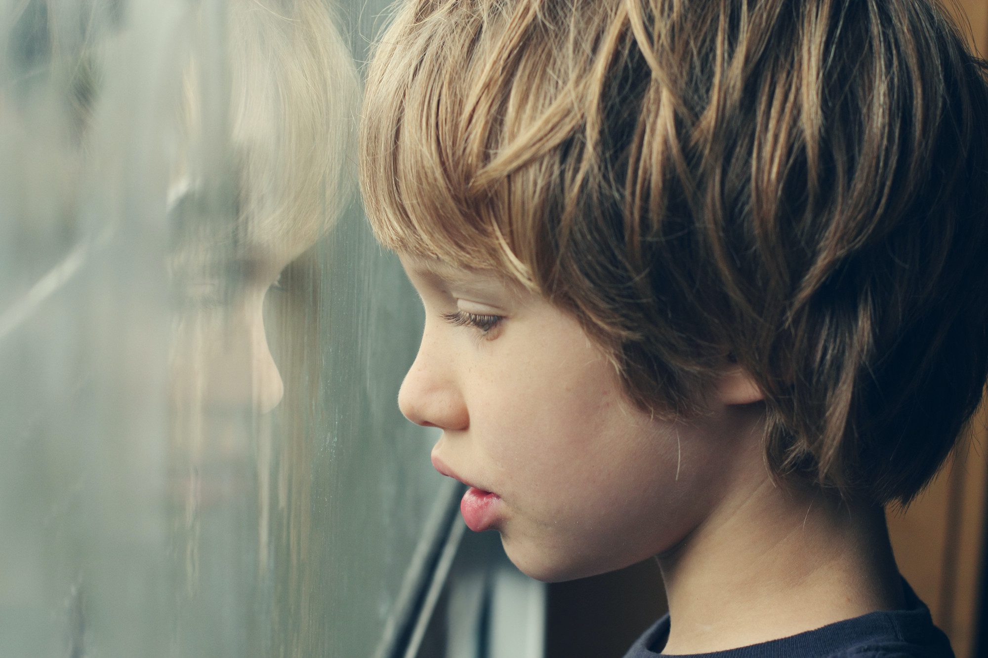 Tired boy staring out his window at gray weather