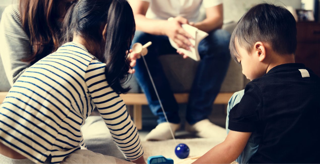 Behind view of two Japanese children sitting on the floor playing in front of their parents