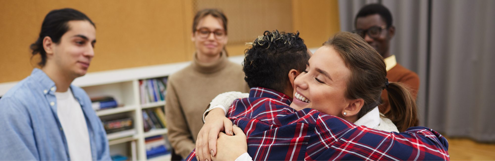 Portrait of two young women hugging in support group meeting, both smiling happily, copy space