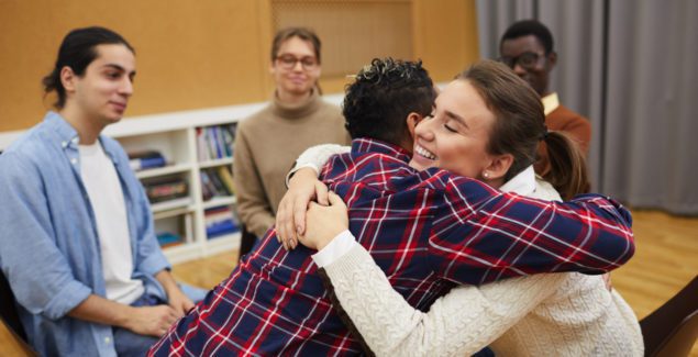 12 Step Program - Portrait of two young women hugging in support group meeting, both smiling happily, copy space