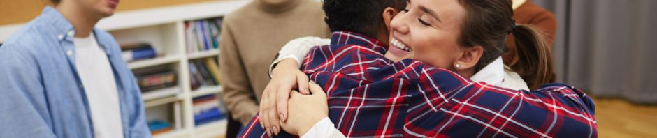 12 Step Program - Portrait of two young women hugging in support group meeting, both smiling happily, copy space
