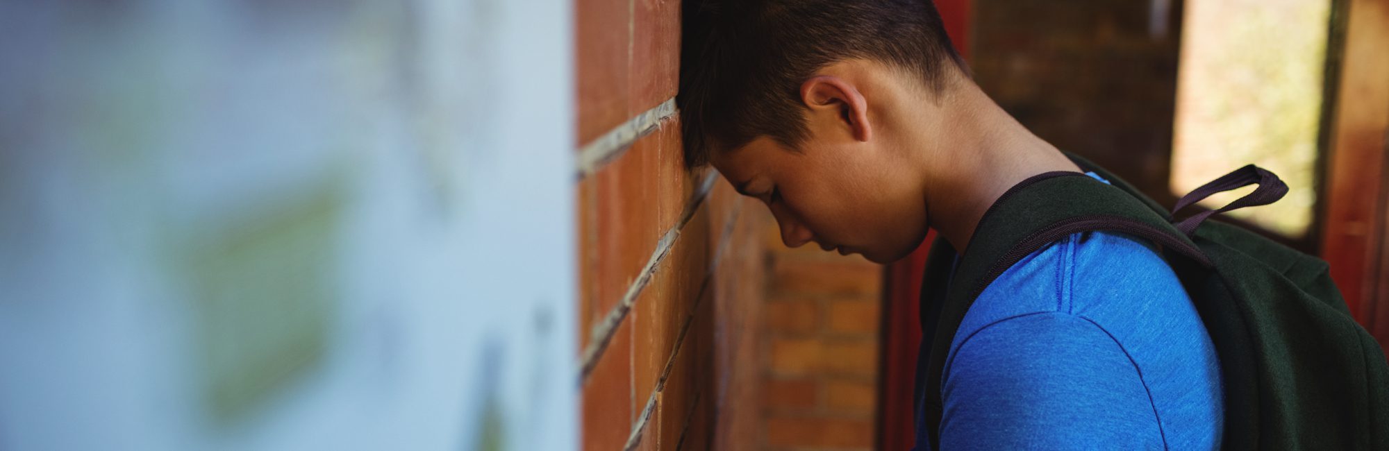 sad schoolboy leaning on brick wall