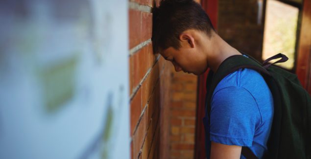 Child in crisis - sad schoolboy leaning on brick wall