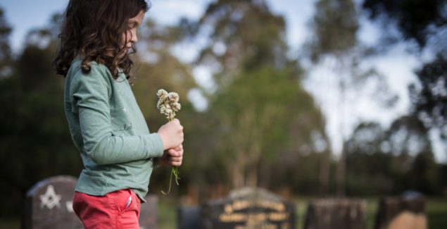 Death of a parent or loved one - young girl standing in cemetery with flower bouquet, looking down sadly