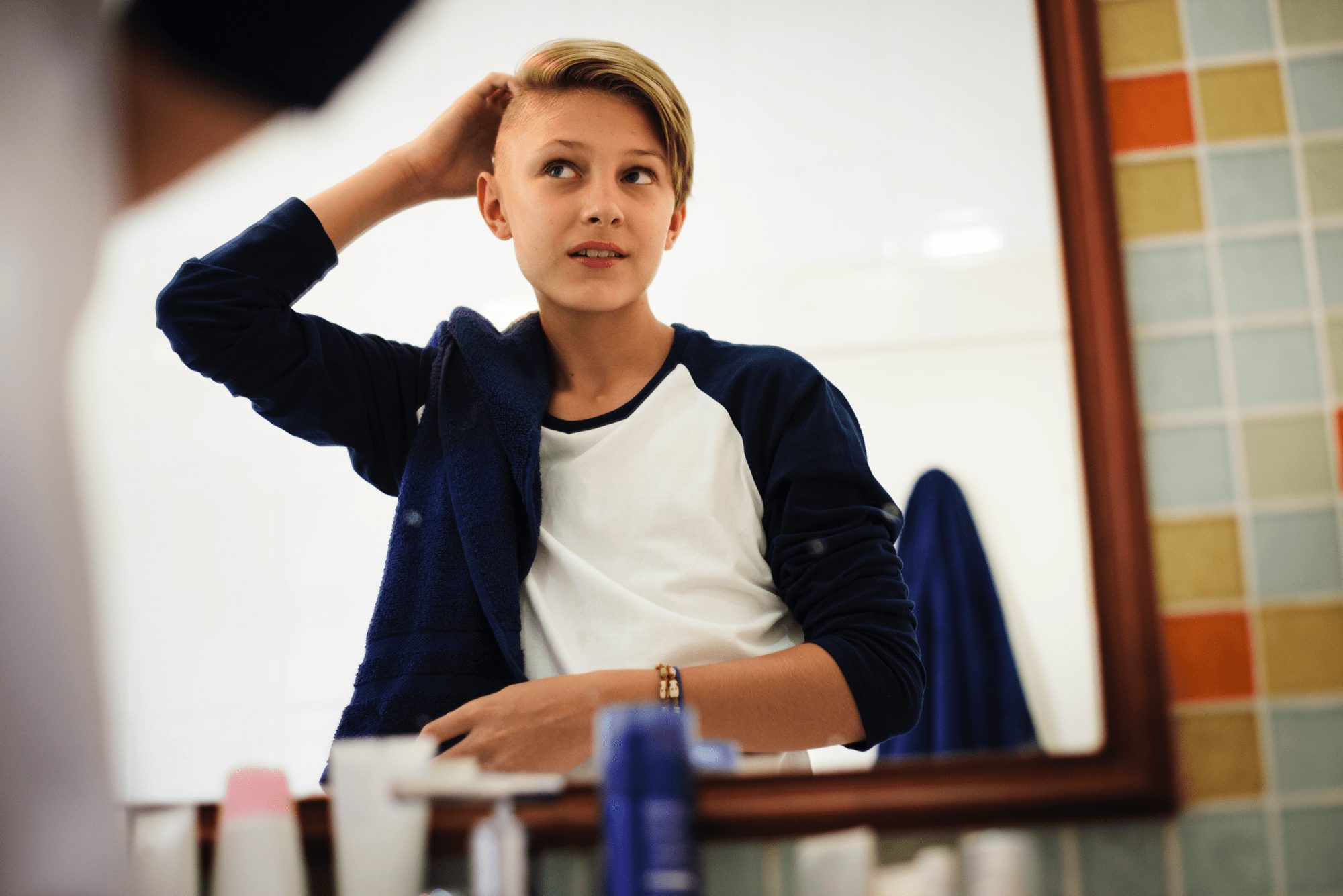 Young caucasian boy set hair with mirror in bathroom