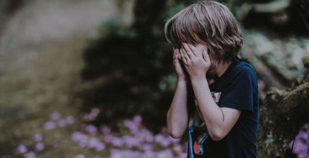 Explosive Child - Young child standing outside with hands firmly covering their face. Gray tone to photograph