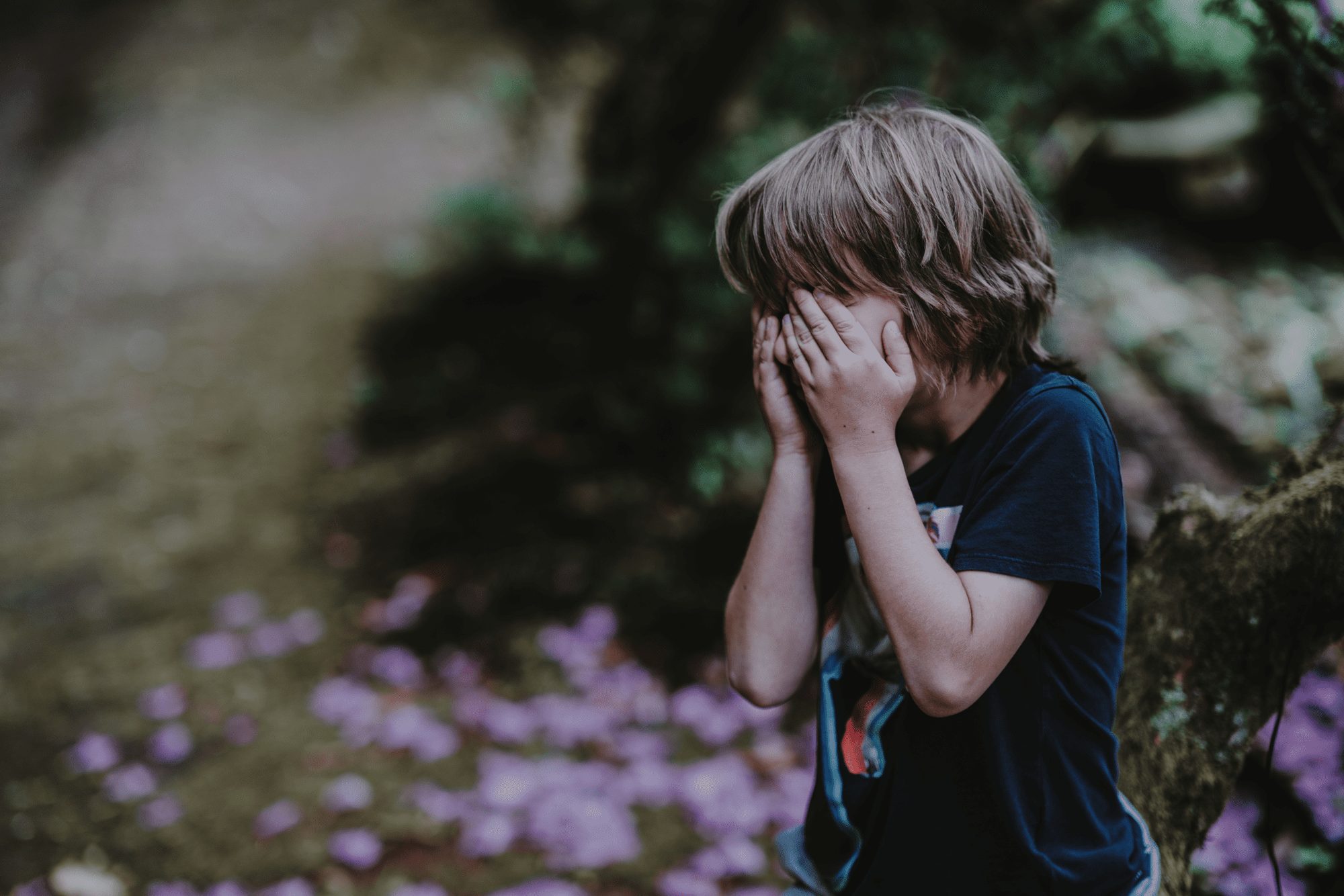 Explosive Child - Young child standing outside with hands firmly covering their face. Gray tone to photograph