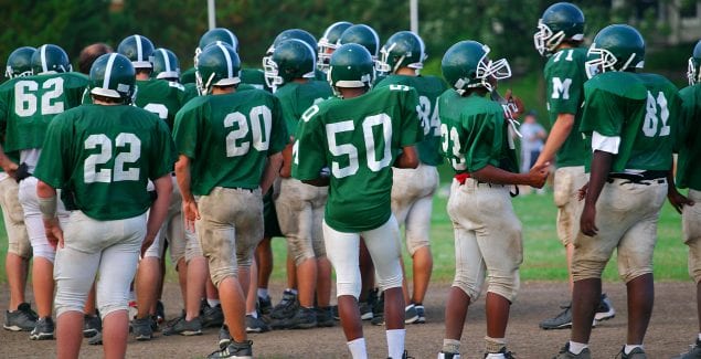 Teenagers on a football team wait for their turn on the field