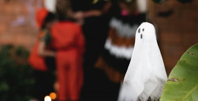 Ghost decoration in foreground of kids trick-or-treating