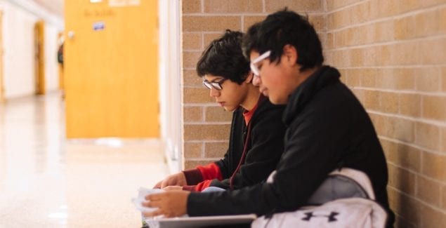 Two Latinx boys sitting in a school hallway together