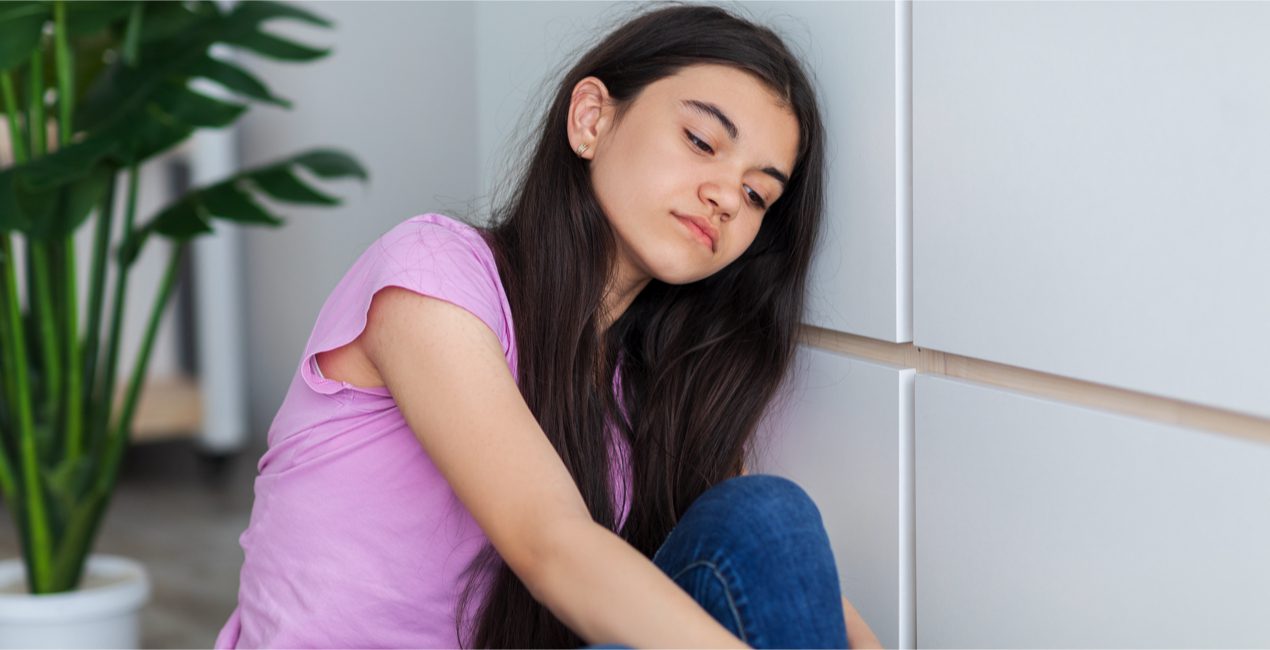 Mental Illness - Portrait of Indian teen girl sitting near wall, feeling unhappy and depressed at home.