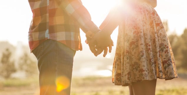 View of two young from the side, facing each other holding hands in front of the shining setting sun