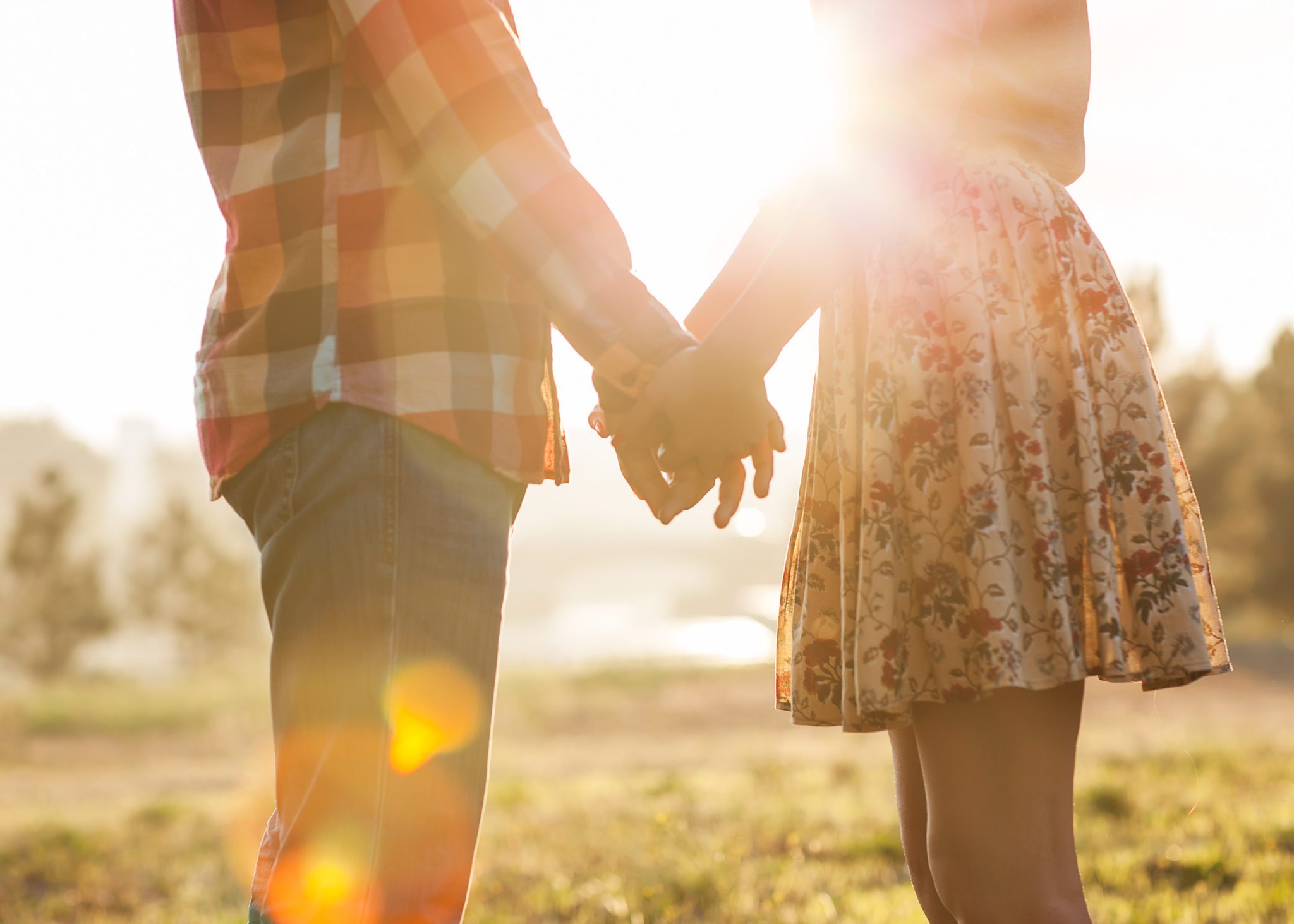 View of two young from the side, facing each other holding hands in front of the shining setting sun