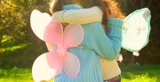 Behind shot of two children wearing fairy wings hugging each other