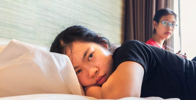 two asian teenager in bedroom, one sister laying in bed and the other sister sitting by the window, having conflict opinion