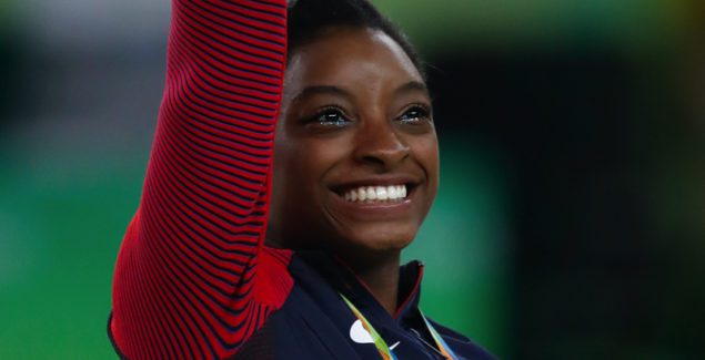 Simone Biles waving and smiling at the 2016 Rio Olympics