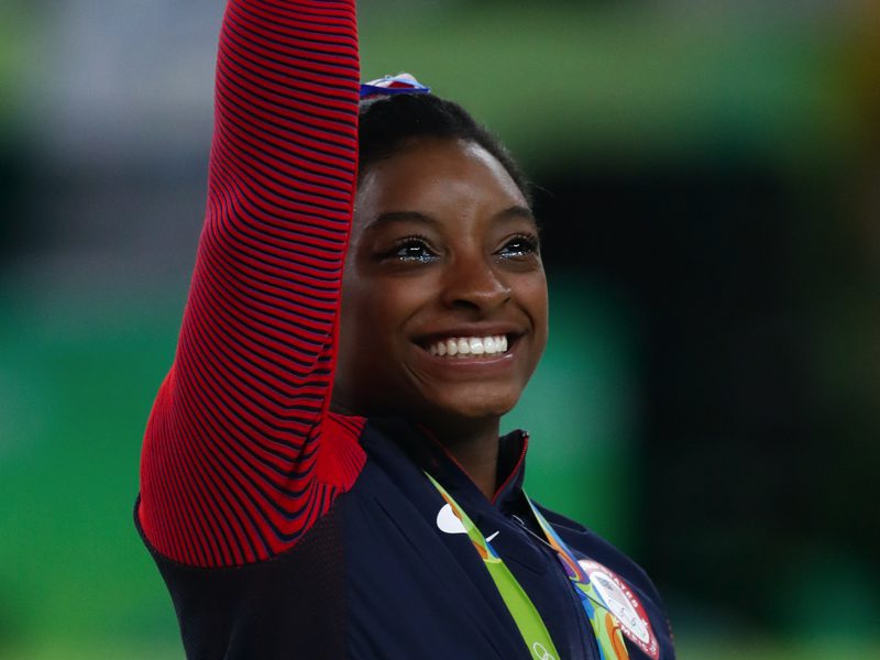 Simone Biles waving and smiling at the 2016 Rio Olympics