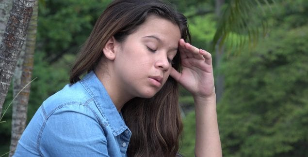 Distraught teen girl, with eyes closed and hand to head