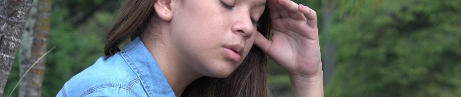 Distraught teen girl, with eyes closed and hand to head