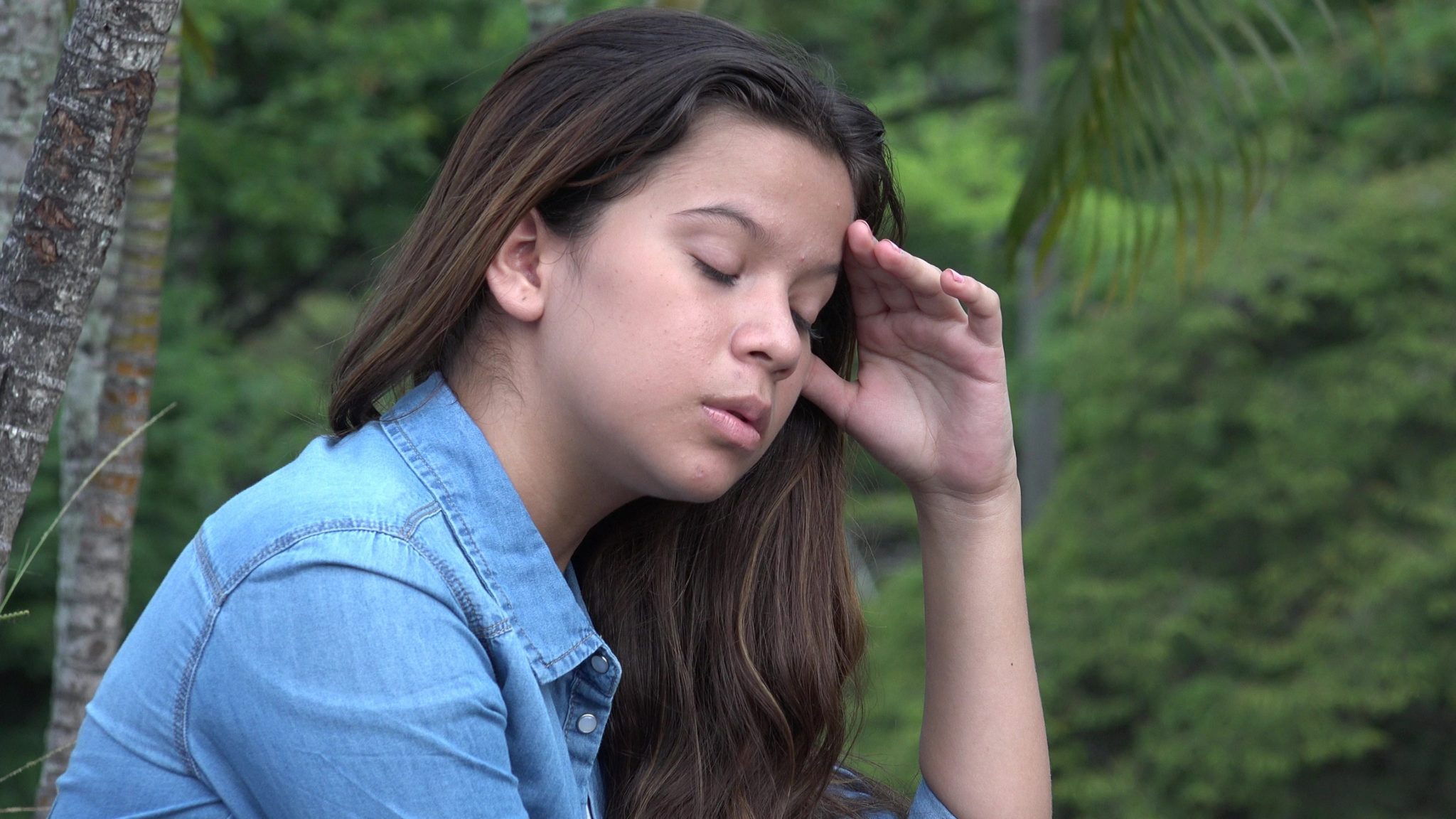 Distraught teen girl, with eyes closed and hand to head