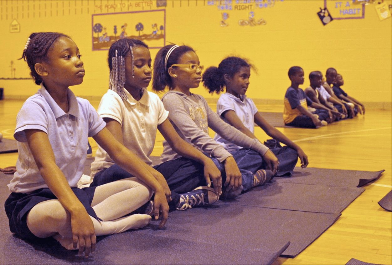 Four young students sitting side by side on mats