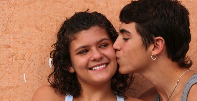 Young teen girl smiling while young teen boy kisses her cheek