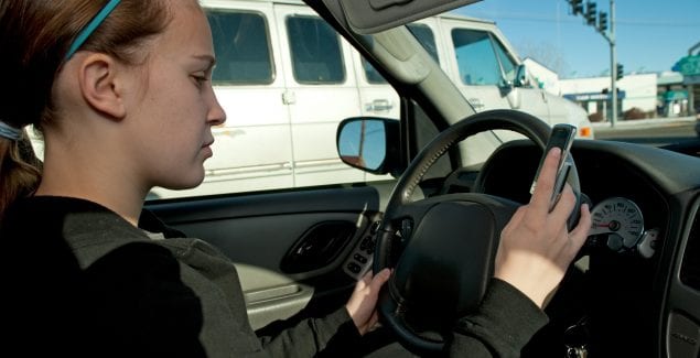 Girl texting with cell phone while driving, hand on steering wheel