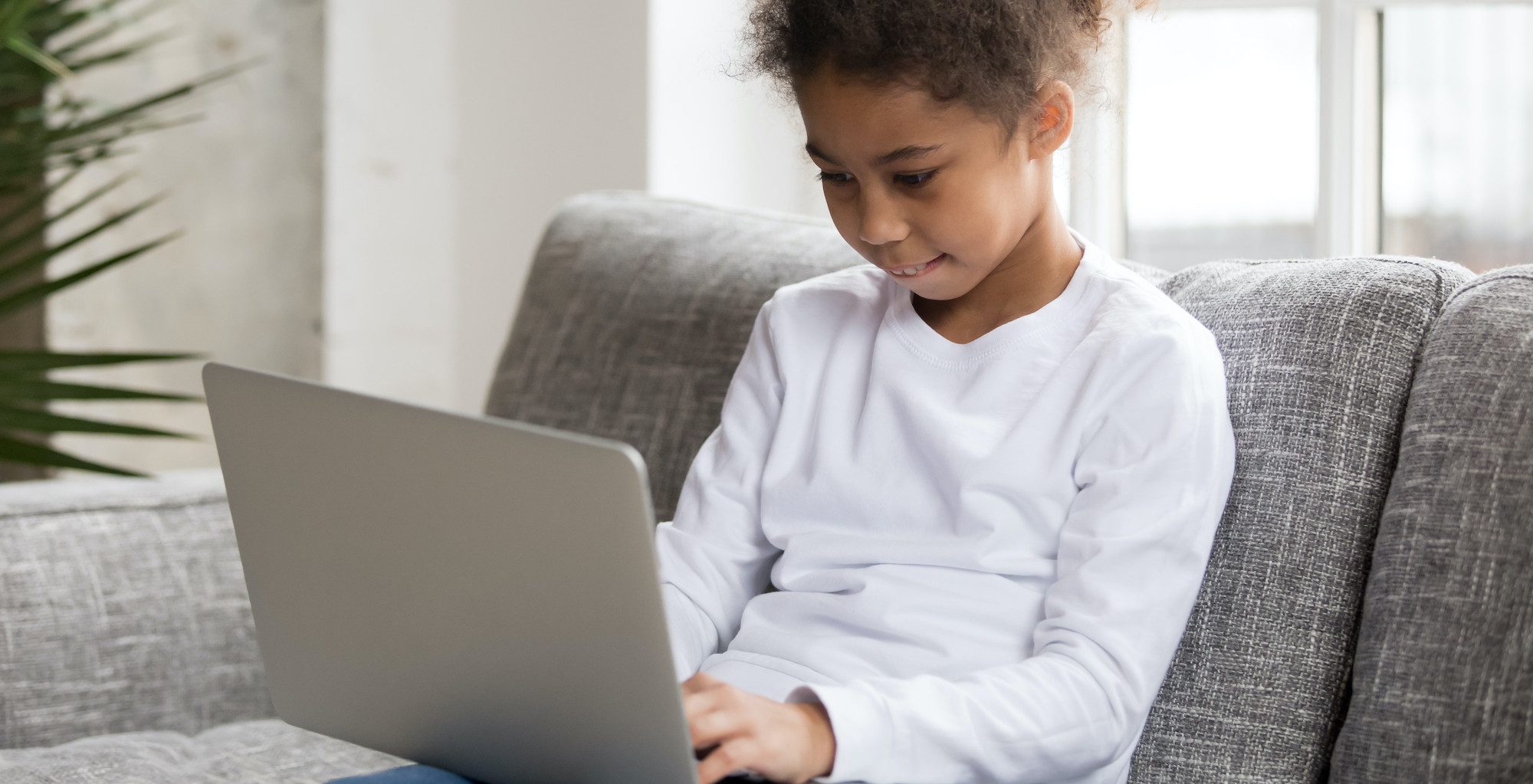 Curious preschool african mixed race girl using laptop on couch, little smart black kid typing on computer chatting with friends online alone at home, child security, children and gadget concept