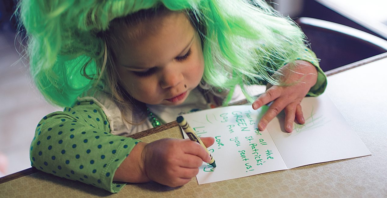 Toddler wearing a green wig while writing a thank you note