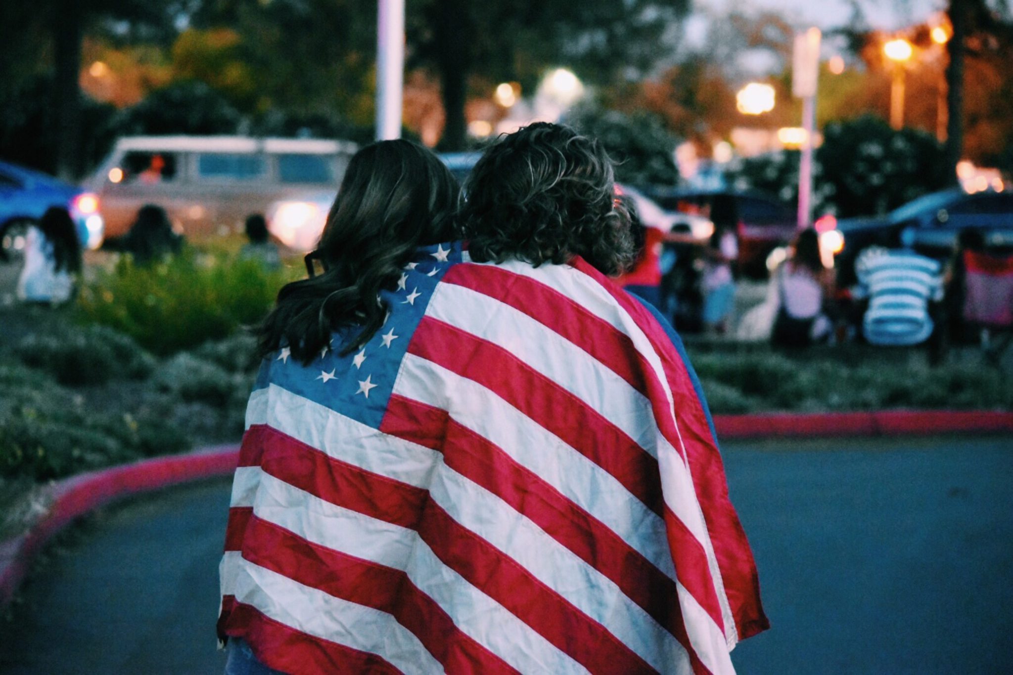 Two individuals walking with backs to camera, draped in American flag