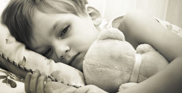 Sepia tone photo of young child cuddling their teddy in bed - measles, flu