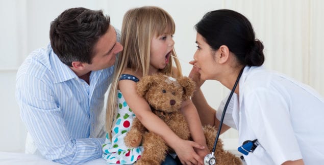 Doctor examining child's throat during a check-up, with parent in the room