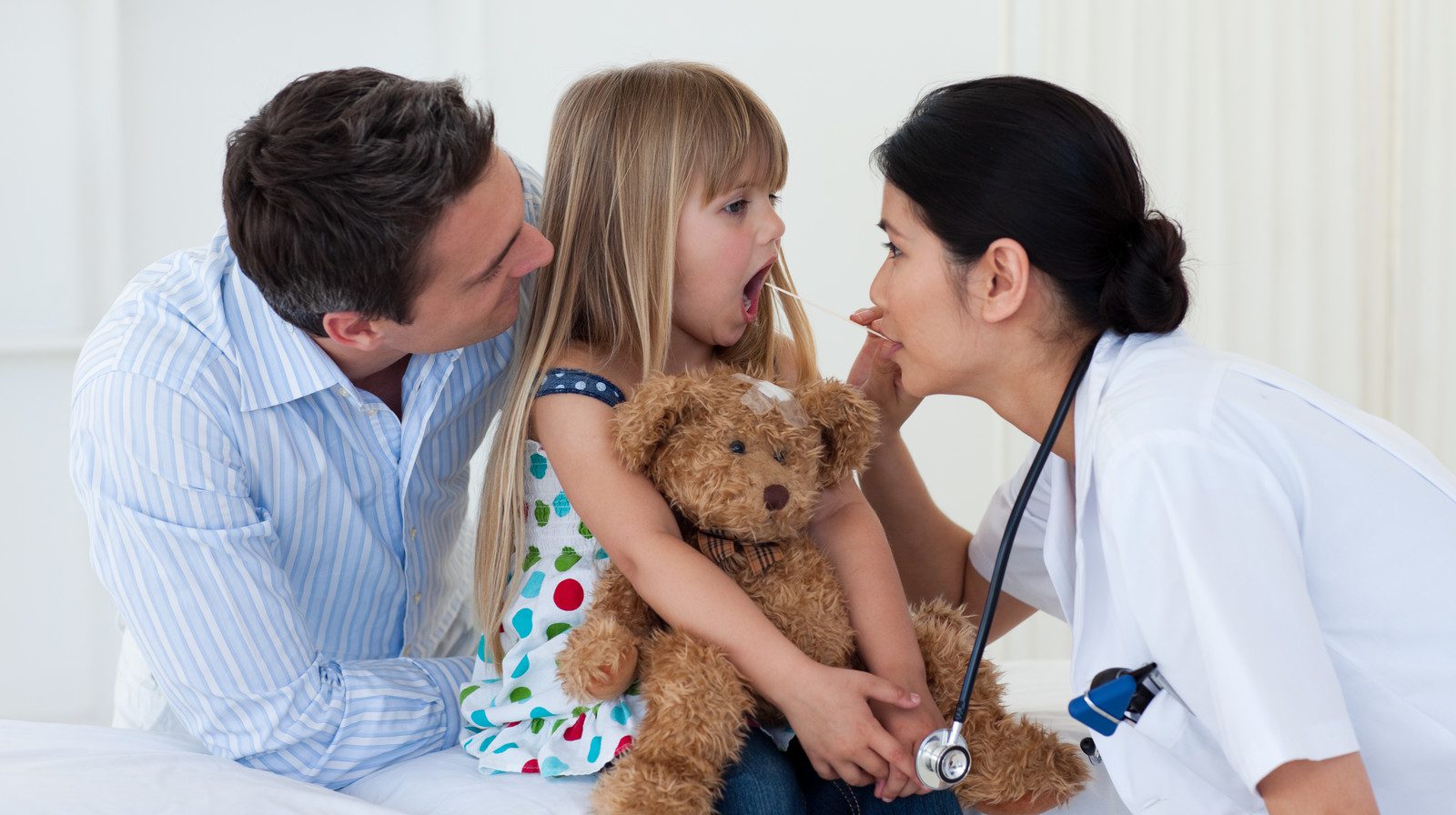 Doctor examining child's throat during a check-up, with parent in the room