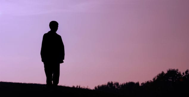 Boy standing alone on a hill dark silhouette over evening sky