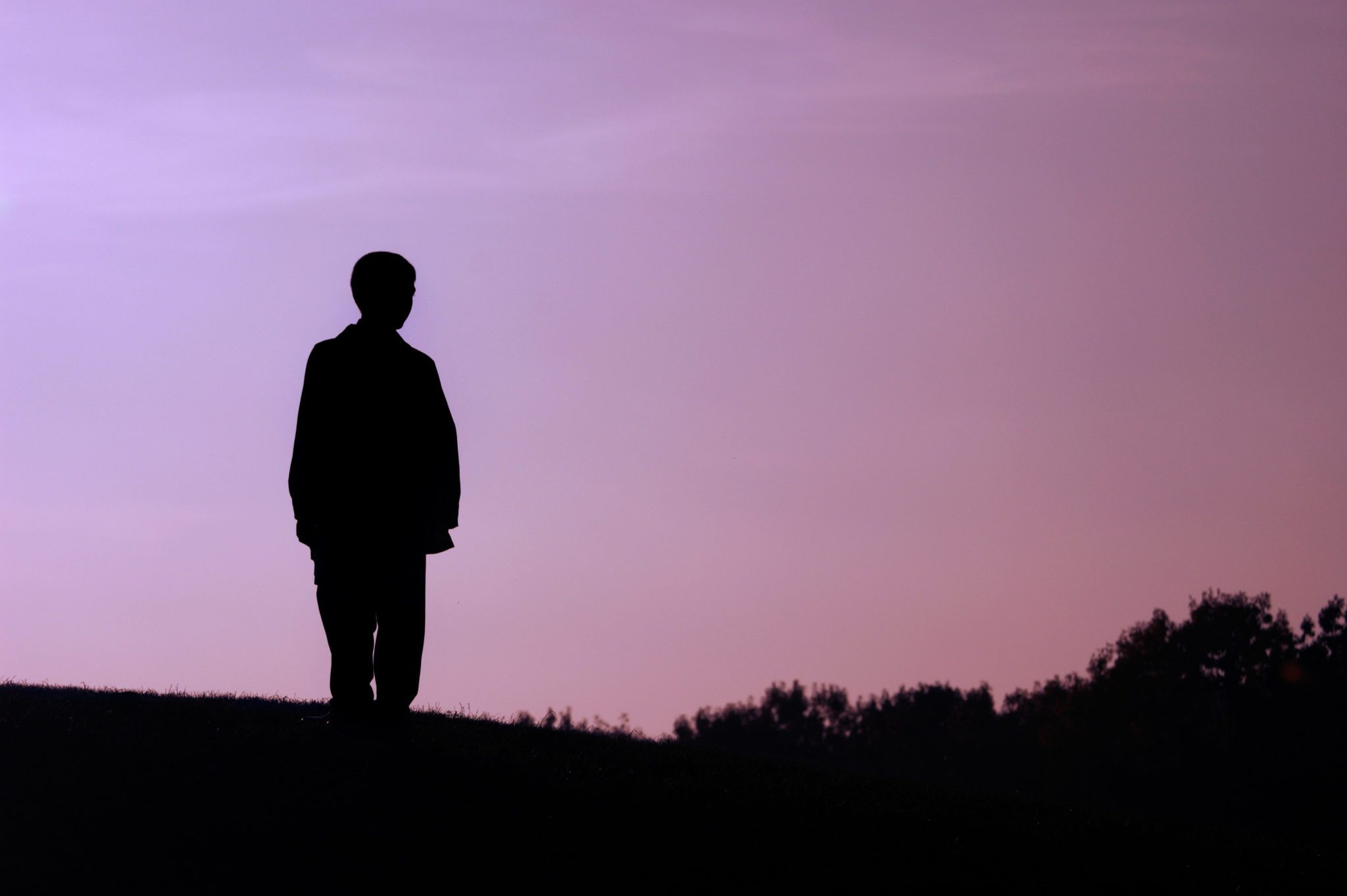 Boy standing alone on a hill dark silhouette over evening sky