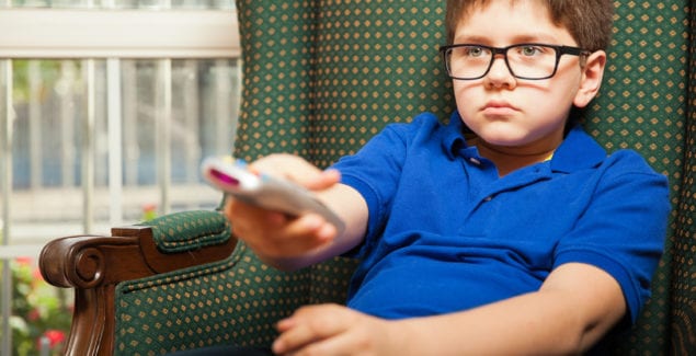 Young male child sitting leaning back on sofa flipping through channels