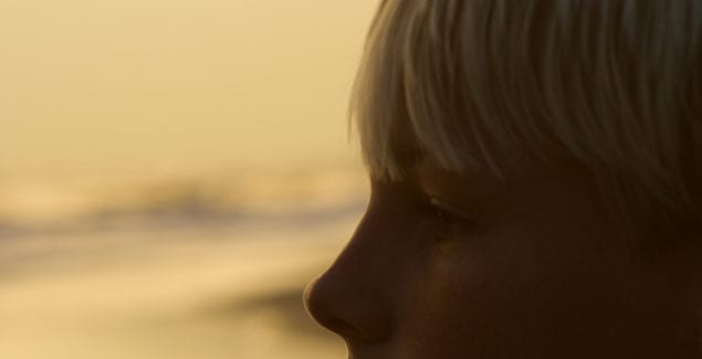 Child Stress - Profile of caucasian pre-teen boy on beach at sunset.