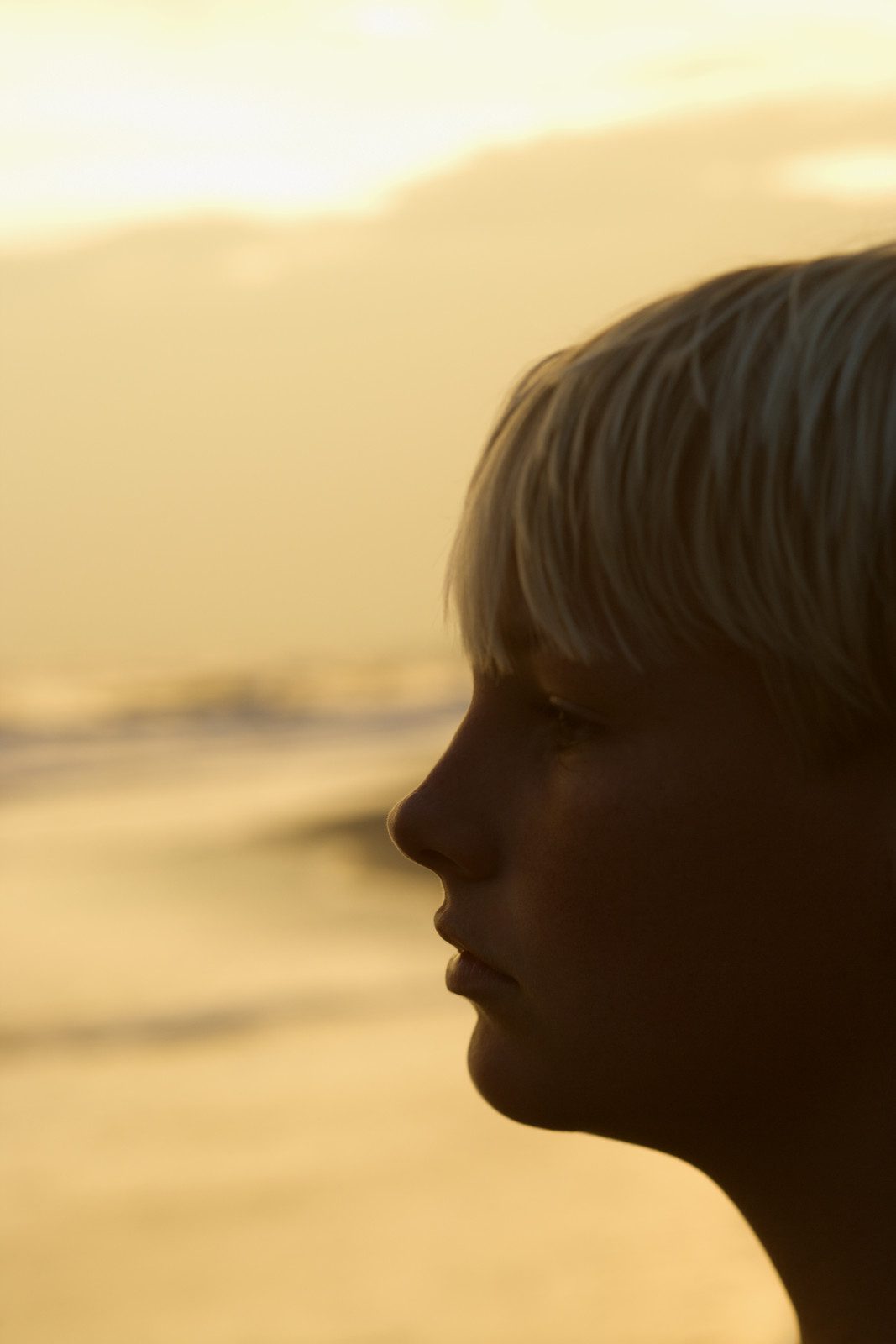 Child Stress - Profile of caucasian pre-teen boy on beach at sunset.