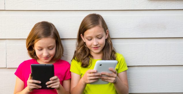 Twin sister girls playing with tablet pc happy on white wall looking screen