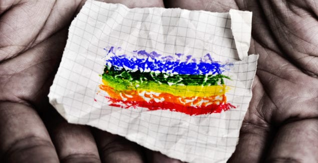 closeup of a young caucasian man with a piece of paper in his hands with a rainbow flag painted in it
