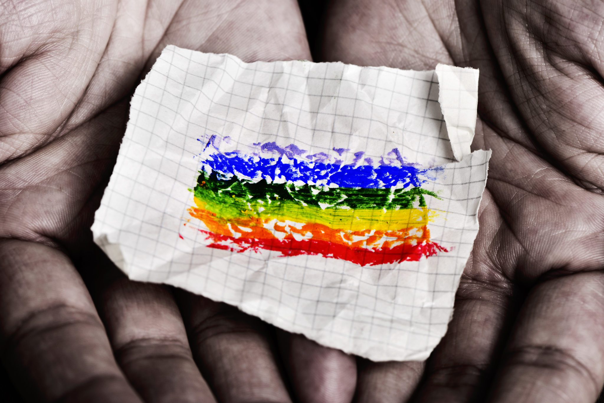 closeup of a young caucasian man with a piece of paper in his hands with a rainbow flag painted in it
